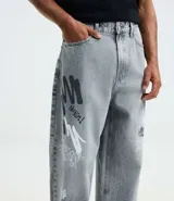 Pantalón de jeans para hombre, modelo super baggy, color celeste desgastado, con estampa de grafiti en negro en ambas piernas. Presenta cintura con trabilla, cierre tradicional y bolsillos.