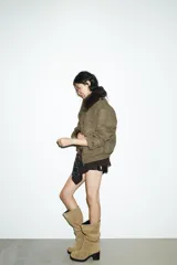 Cazadora color verde militar con efecto ante, cuello solapa con aplicación de pelo sintético desmontable, manga larga con puño, trabillas en los hombros y bolsillos frontales con solapa y botón. Cierre frontal con cremallera y botones ocultos.