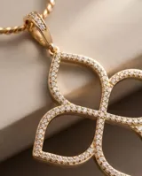 Collar de bronce con baño de oro, compuesto por una cadena fina y un dije colgante en forma de trébol de cuatro hojas o flor, adornado con circonias incrustadas.