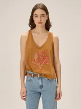 Remera de algodón con escote en V, sin mangas, de corte cómodo y color tostado, con un detalle artesanal de flor bordada en el frente.