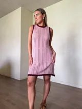 Vestido corto de punto tejido con hilo de algodón, color rosado con detalles en bordó en el cuello redondo y los bordes sin mangas. Presenta un diseño recto con calados en franjas horizontales y terminación con ondas.