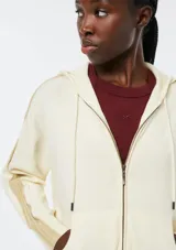 Campera de punto con cierre frontal, capucha con cordones ajustables y bolsillos tipo canguro. Presenta un diseño de manga larga con detalles acanalados en los laterales y puños.