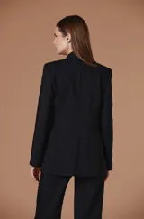 Saco negro de corte sastre con solapas tipo chal y cierre frontal mediante lazada. Presenta detalles de encaje o bordado texturizado en las mangas y en las solapas de los bolsillos laterales.
