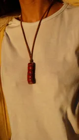 Collar con dije cilíndrico de coral rojo natural, montado sobre un cordón de cuero marrón.