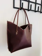 Cartera de cuero color marrón chocolate con manijas largas y borde superior en corte en V. Diseño amplio y liviano, con terminaciones artesanales y costuras contrastantes en todo el contorno.
