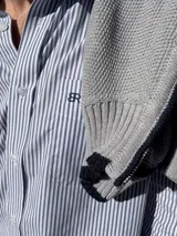 Camisa de corte clásico confeccionada en algodón, con diseño de rayas verticales finas en color rosa sobre fondo blanco. Presenta cuello abotonado, cierre frontal con botones, mangas largas con puños abotonados y un bolsillo en el pecho con el logo de la marca bordado.