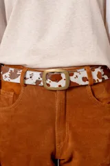Cinturón de cuero con acabado de pelo sintético estampado con diseño de manchas tipo animal print, con hebilla metálica rectangular en tono bronce envejecido.