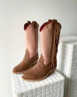Botas estilo tejano de caña alta, confeccionadas en cuero vacuno. Presentan una combinación de colores en beige y marrón texturizado, con detalle de flecos laterales y borde superior en color rojo.
