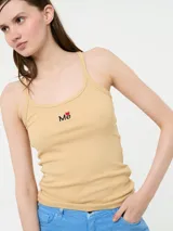 Top de tirantes color beige con tejido acanalado y sisas profundas. Presenta un pequeño emblema bordado con la palabra "Me" y una corona en el frente. El escote es redondeado en la parte delantera y recto en la espalda.