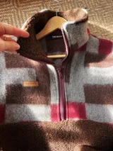 Buzo de abrigo con diseño de bloques, confeccionado en una combinación de corderito marrón y textiles vintage con estampado a cuadros en tonos gris, marrón y bordó. Presenta cuello alto con cierre frontal parcial y mangas largas.