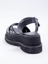 Sandalias negras de plataforma con doble tira cruzada sobre el empeine, tachas plateadas y ajuste con hebilla en el tobillo.