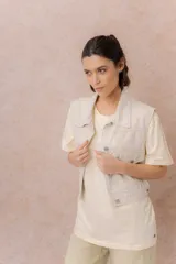 Chaleco de jean color crudo, con calce relajado y largo a la cintura. Cuenta con cuello camisero, cierre frontal con botones metálicos y bolsillos delanteros con tapa.