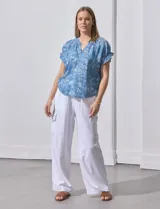 Blusa de lyocell color celeste con estampado de motivos playeros en blanco. Tiene cuello a la base con escote en V, mangas cortas con volados y detalle fruncido en mangas y espalda.
