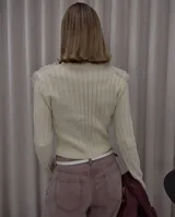 Chaqueta de punto color crema con diseño entallado, cierre frontal completo y mangas largas acanaladas. Presenta un detalle de textura tipo bouclé o flecos en la parte frontal superior.
