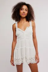 Mini vestido slip blanco de tela liviana y fruncida, con escote en V, tirantes anchos de encaje y detalles de encaje translúcido en el bajo. Silueta entallada en el busto y falda corta con vuelo.