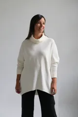 Polerón de punto color crudo, con cuello alto tipo polera, corte holgado y mangas largas con puños acanalados.