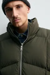 Cazadora acolchada de corte relajado confeccionada en tejido técnico color verde militar. Presenta cuello subido, cierre frontal con cremallera, mangas largas con puños elásticos y bolsillos frontales con cremallera oculta.
