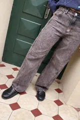 Pantalón de jean de corte recto y tiro medio, con un acabado de teñido ácido en tonos oscuros. Presenta bolsillos traseros con bordados decorativos en color negro y una etiqueta de cuero en la cintura.