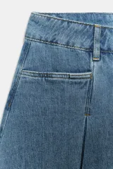 Falda corta de tiro medio confeccionada en tejido denim de algodón. Presenta diseño con tablas, bolsillos delanteros, cintura con trabillas y bajo desflecado. Cierre frontal con cremallera, botón y ganchos metálicos.