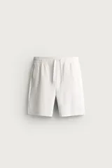 Bermuda regular fit de tejido elástico color blanco, con cintura elástica ajustable mediante cordón, bolsillos delanteros y bolsillos traseros de vivo.