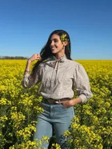 Blusa de manga larga con estampado de cuadros vichy en tonos azul y blanco, cuello alto con volados y lazo para anudar, pliegues frontales y cierre con botones nacarados.