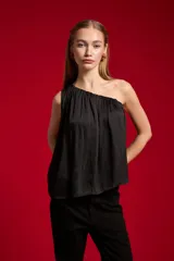 Blusa de poliéster color negro, con diseño asimétrico de un solo hombro, plisado ligero y corte holgado.