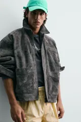 Cazadora de corte relajado confeccionada en piel con acabado de serraje. Presenta cuello solapa, cierre frontal con cremallera oculta bajo solapa con botones a presión, bolsillo con cremallera en el pecho y bolsillos de plastrón con solapa en la cadera. Incluye efecto vintage en las costuras y puños con botón.