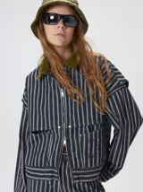 Campera de denim a rayas verticales con cuello de pana en color bordó. Presenta cierre frontal, mangas desmontables con cierre en los hombros, canesú en el pecho y bolsillos de parche cuadrados.