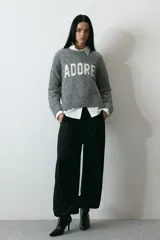 Buzo de punto gris melange con diseño jacquard y la palabra 'ADORE' en blanco en el frente, cuello redondo y hombros caídos.