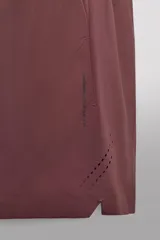 Pantalones cortos deportivos color marrón rojizo, confeccionados en tejido técnico ligero y elástico. Presentan cintura elástica ajustable con cordón interior, bolsillos frontales y un bolsillo trasero con cierre de cremallera. Los laterales tienen perforaciones para transpirabilidad y aberturas laterales en el bajo.
