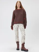 Sweater de punto con diseño de ochos en color verde, cuello redondo con detalle de franja en contraste, y apliques de rombos en las mangas. Presenta un bordado con la letra M en el pecho.