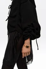 Cárdigan de punto negro con diseño amplio, escote redondo, cierre frontal mediante lazos y mangas largas con detalles de lazos ajustables en los puños.
