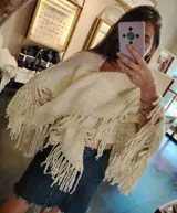 Ruana triangular tejida a crochet color crema con flecos largos.