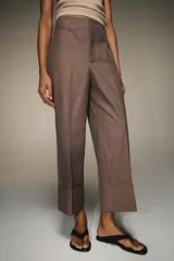 Pantalón marrón de tiro alto con bolsillos delanteros y traseros. El bajo está acabado con vuelta. Cierre frontal con cremallera y ganchos metálicos.