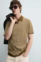 Polo de punto de algodón con corte regular fit, manga corta y cuello solapa con abertura frontal en forma de V. Presenta un diseño a rayas horizontales marrones y beige, con ribetes en color marrón oscuro en el cuello, puños y bajo.