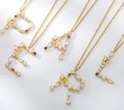 Cadena dorada con dije de letra grande, con piedras y perlas engarzadas.