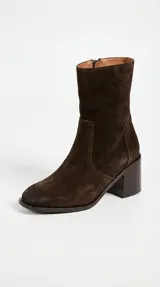 Bota de caña media confeccionada en cuero vacuno color marrón oscuro, con taco cuadrado de madera y punta cuadrada. Presenta cierre lateral interno y elástico en la caña para mayor ajuste.