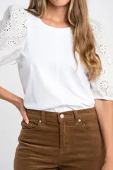 Remera de algodón color rosado con mangas cortas abullonadas de broderie con diseño floral calado. Presenta cuello redondo y costura vertical central en el frente.