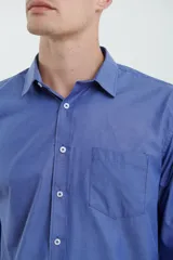 Camisa azul de manga larga con cuello clásico, cierre con botones y bolsillo en el pecho.