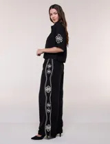 Conjunto de dos piezas negro compuesto por camisa de manga corta con cuello camisero y pantalón palazzo de tiro alto. Presenta detalles de bordados florales en contraste a lo largo de los laterales del pantalón y en las mangas.