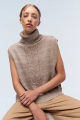 Chaleco de punto color beige, con cuello alto y diseño trenzado en el centro.