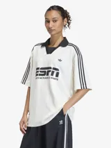 Camiseta de fútbol de corte oversize, color blanco con detalles en negro. Presenta cuello tipo polo con escote en V, mangas cortas con las icónicas tres tiras de Adidas en los hombros y estampado gráfico frontal inspirado en la estética deportiva de los años 90.