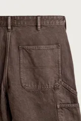 Pantalón jeans relaxed fit de color marrón con efecto lavado, de corte recto y estilo carpintero. Cuenta con bolsillos laterales, bolsillos traseros, bolsillos aplicados y tira multifunción en la pierna. Cierre frontal con cremallera y botón metálico.