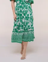 Vestido midi de estilo bohemio en color verde y blanco, con estampa floral, escote en V, cierre frontal con botones, mangas cortas amplias, cintura ajustable con lazo y volado en el bajo.