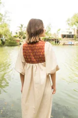 Túnica de lino color crudo con corte holgado y mangas abullonadas con elástico. Presenta una pechera frontal y trasera con estampado étnico en tonos terracota y amarillo.