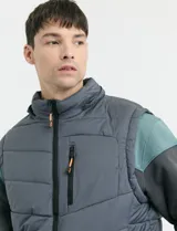 Chaleco capitoneado de color azul marino, con capucha desmontable, cierre frontal y bolsillos laterales con detalles en naranja. Presenta un diseño acolchado con costuras horizontales.