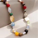 Collar de cuentas multicolor con piedras de diversas formas, tamaños y texturas, intercaladas con pequeñas esferas doradas.