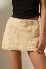 Falda mini de color crema, confeccionada con una base de lentejuelas pequeñas y decorada con aplicaciones de lentejuelas circulares de mayor tamaño en relieve.