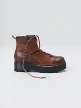 Bota de estilo trekking con diseño multicolor en tonos marrón, azul y detalles en rojo. Presenta plataforma de goma dentada, cordones tipo cuerda de escalada y cuello acolchado.