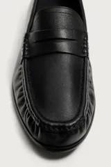 Mocasín de vestir negro confeccionado en piel, con detalle fruncido en la parte delantera y antifaz en el empeine. Cuenta con suela a tono y ligero tacón.